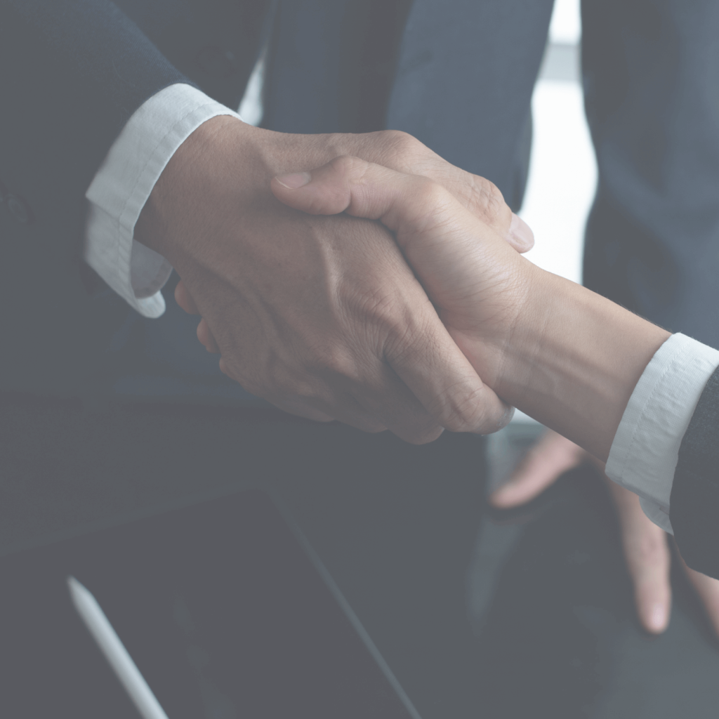 Close-up of two people in business suits shaking hands in an office setting.